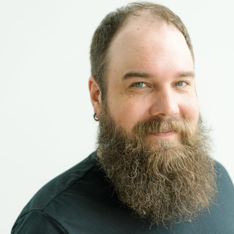 headshot-style photo of D'nelle, wearing a black jacket and blue camisole.